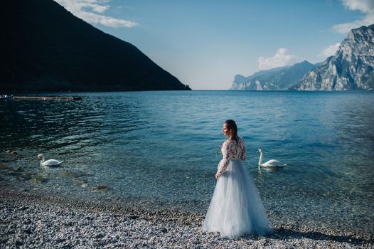 a girl in a smart white dress walks along the embankment of lake Garda.A woman is photographed against the background of a mountain and lake in Italy.Torbole.