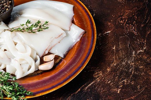 Sliced raw rings Calamari in a rustic plate with rosemary. Dark background. Top view. Copy space.