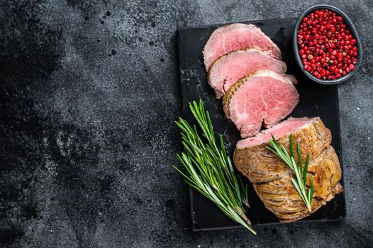 Roast beef fillet Tenderloin meat on a marble board. Black background. Top view. Copy space.