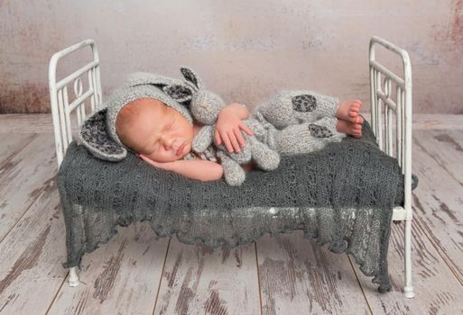 baby sleeping on a bed, in a gray knitted suit with a lovely toy of a bunny