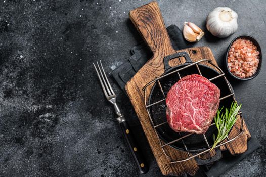 Raw fillet mignon beef steak on a grill with herbs. Black background. Top view. Copy space.