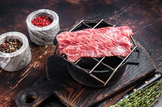 Premium raw sliced wagyu beef A5 steaks on a grill for yakiniku. Japanese foods. Dark background. Top view.