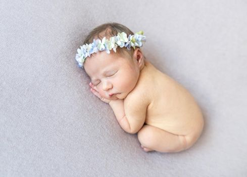 Naked infant sleeping curled up, wearing a cute headband with flowers, white background