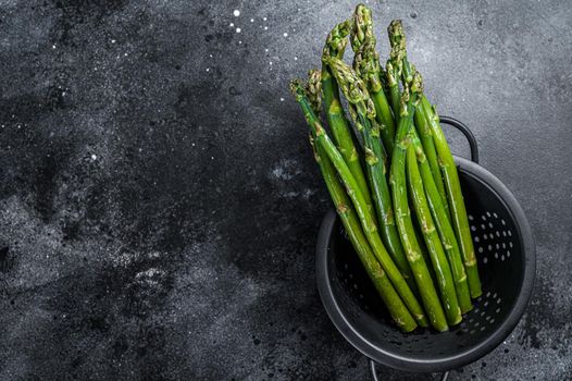 Raw green asparagus in a old colander. Black background. Top view. Copy space.