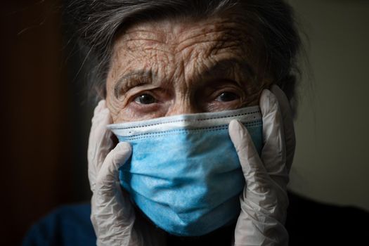 Sad senior woman in protective mask, latex gloves at home during coronavirus pandemic. Stay at home. Old granny retired quarantined epidemic covid 19. Gray hair female in mask infection, bacteria flu.