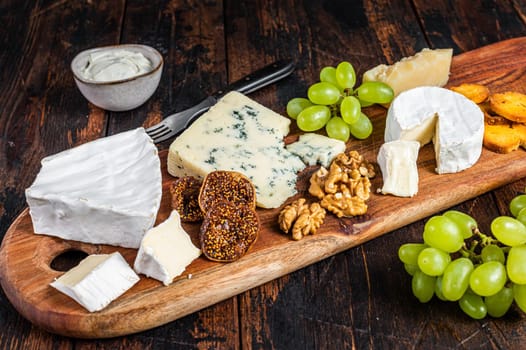 Assorted Cheese board with Brie, Camembert, Roquefort, parmesan, blue cream cheese, grape and nuts. Dark wooden background. Top view.