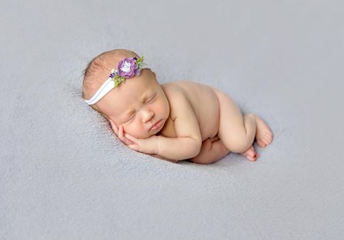 Naked baby girl wearing flowery hairband sleeping on her side, hands pressed to the cheek