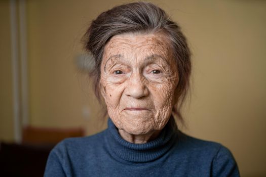 Elderly Caucasian senior grandmother ninety years old looks attentively and smiles, feels happy, large portrait, face with deep wrinkles, gray hair. Theme pensioners, old people and long-lived woman.