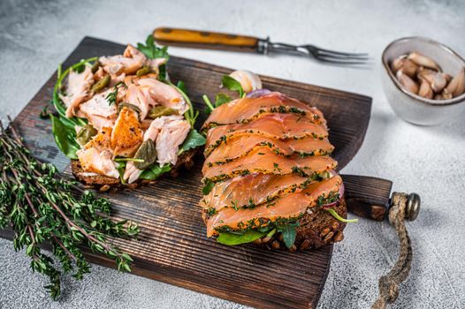 Sandwich toast with hot and cold smoked salmon, arugula and cream cheese on a wooden board. White background. Top view.