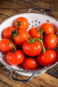 Branch of Red cherry tomatoes in colander. Wooden background. Top view.