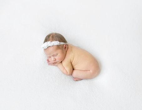 Naked infant sleeping curled up, wearing a cute headband with flowers, white background