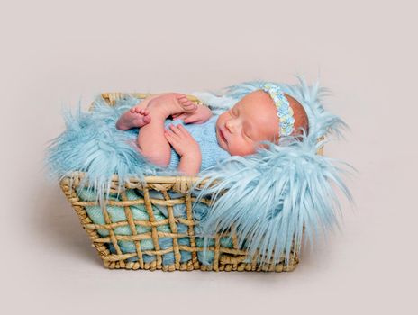 Happy newborn girl lying on her back and cuddling her toy. Little girl wearing blue headband and blue bodysuit lying on blue flokati rug and smiles in sleep while hugging her hare toy