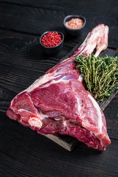 Uncooked Raw lamb mutton leg with herbs on butcher cutting board. Black wooden background. Top view.