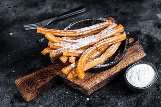 Traditional Mexican dessert churros with sugar powder in a pan. Black background. Top view.