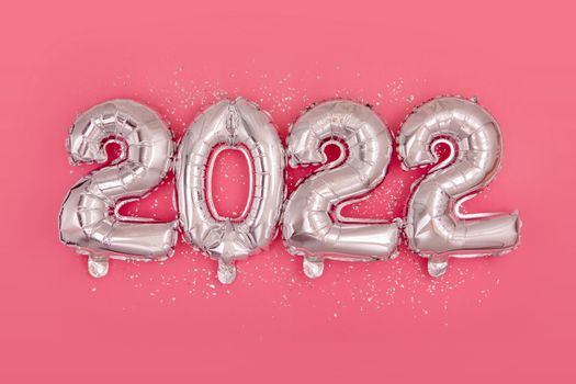 Silver foil balloons numeral 2022 and confetti on pink background Happy New year 2022 celebration Flat lay