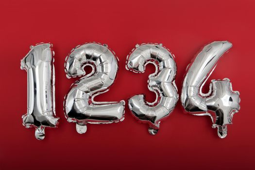 Top view of shiny silver number balloons arranged in row from 1 to 4 on red background
