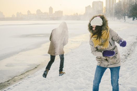 Young Caucasian people in love heterosexual couple have a date in winter near a frozen lake. Active holiday holiday Valentine's Day, playing snowballs and playing joy.