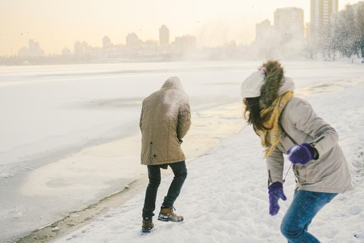 Young Caucasian people in love heterosexual couple have a date in winter near a frozen lake. Active holiday holiday Valentine's Day, playing snowballs and playing joy.