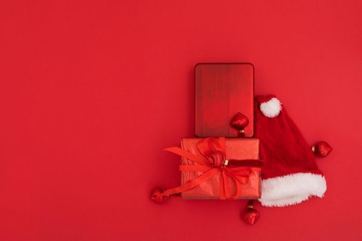 Top view of composition of traditional Santa hat placed near wrapped gifts on Christmas day against red background