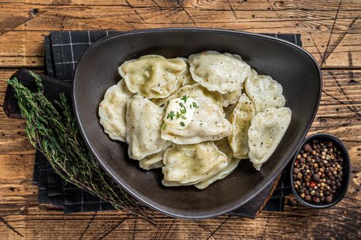 Dumplings pierogi with potato in a plate with herbs and butter. Wooden background. Top View.