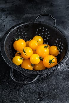 Yellow cherry tomato in a colander. Black background. Top view.