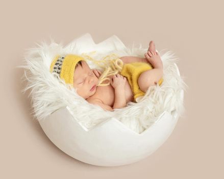 funny sleeping baby in yellow romper with chicken toy on round cot, top, view