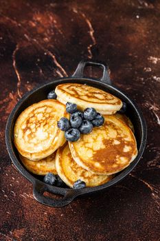 Fried Pancakes with fresh blueberries and maple syrup in a pan. Dark background. Top View.