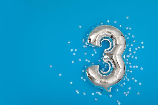 Silver balloon 3 on a blue background with confetti stars. Number three 3. Holiday Party Decoration or postcard concept with top view on blue background