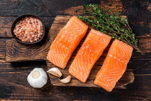 Fresh Raw salmon fish fillet steaks on wooden board with thyme. Dark wooden background. Top view.