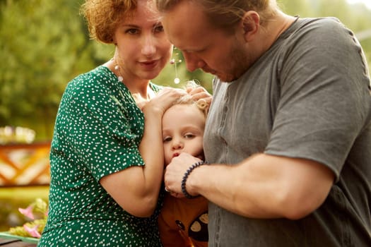 Crop caring mother and father in casual wear playing with cute son while standing together in rural area with lush green trees