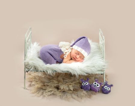 Cute little baby in white and purple knitted suit sweetly sleeping in small bed