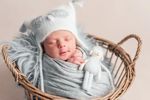 Top view of baby in white knitted hat sleeping in basket covered in blanket