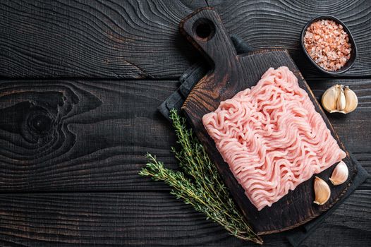 Fresh Raw mince or ground chicken meat on wooden chopping board with thyme. Black wooden background. Top view. Copy space.