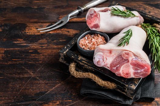 Uncooked Raw pork hoof, knuckle, feet in a wooden tray with herbs. Wooden background. Top view. Copy space.