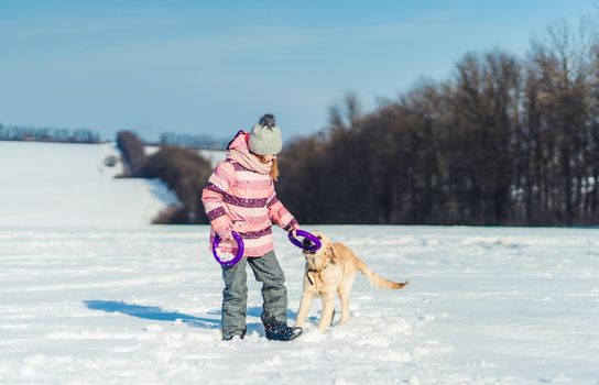 Happy little girl playing with cute dog outside on snowy field