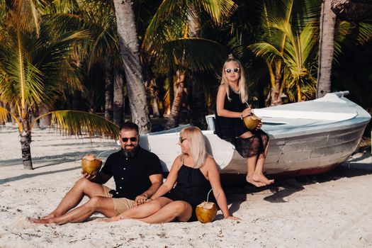 a stylish family in black clothes with coconuts in their hands on the beach of the island of Mauritius.Beautiful family on the island of Mauritius in the Indian ocean.