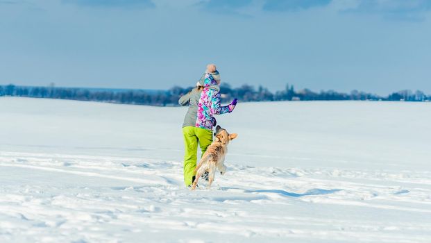 Back view of girl running in snow with dog