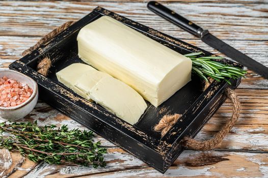 Butter Margarine block in a wooden tray with herbs. White wooden background. Top view.