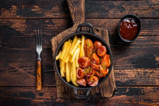 Currywurst street food meal, Curry spice on wursts served French fries in a pan. Dark wooden background. Top view.