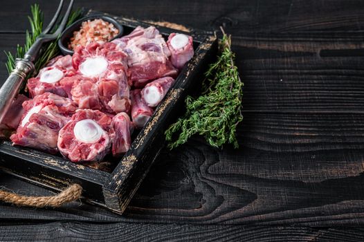 Raw veal beef Oxtail Meat in wooden tray with thyme. Black wooden background. Top view. Copy space.