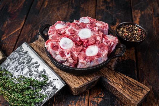 Raw veal beef Oxtail Meat on butcher wooden board with cleaver. Dark wooden background. Top view.