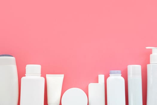 Top view of white plastic cosmetic bottles placed in row on pink background