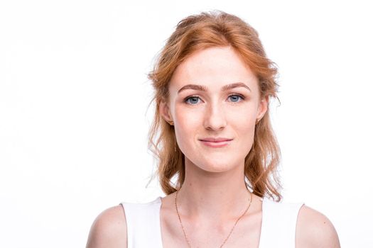 Portrait of a beautiful young woman of European, Caucasian nationality with long red hair and freckles on her face posing on a white background in the studio. Close-up student girl in a white blouse.