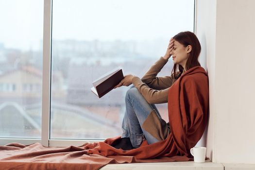 woman with a book near the window with a cup of coffee. High quality photo