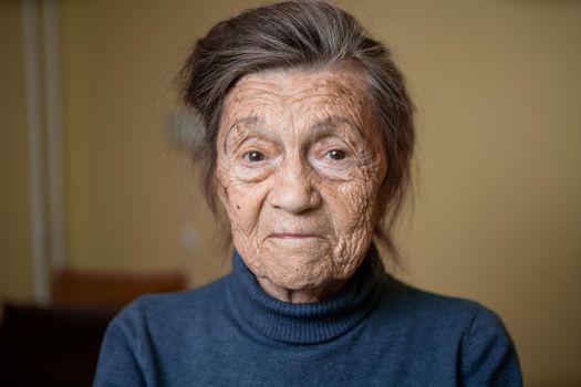Older cute woman of ninety years old Caucasian with gray hair and wrinkled face looks at camera, cute kind look and smiles.Mature grandmother retired long-liver, theme emotion and mood of old people.