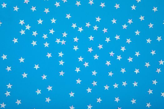 Blue background with shiny iridescent pearl stars. Festive trendy blue background with silver metallic stars