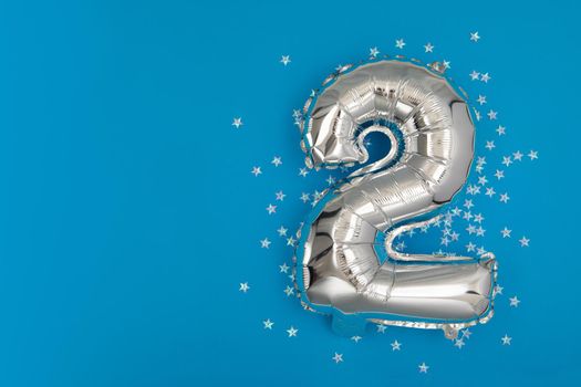 Silver balloon 2 on a blue background with confetti stars. Number two 2. Holiday Party Decoration or postcard concept with top view on blue background