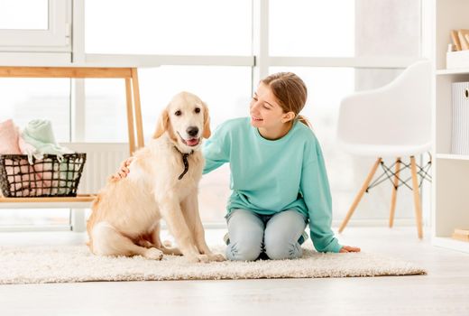 Smiling girl with lovely young dog sitting on floor in light room