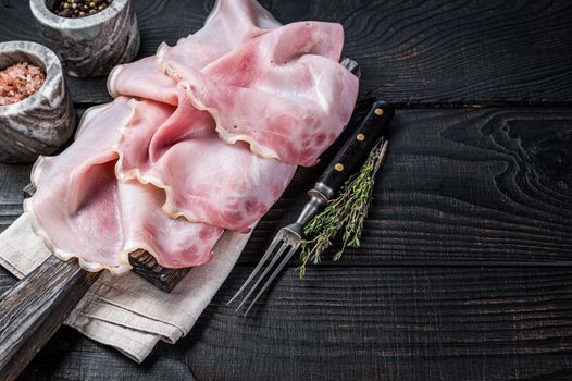 Sliced prosciutto ham on wooden board with herbs. Black wooden background. Top view. Copy space.