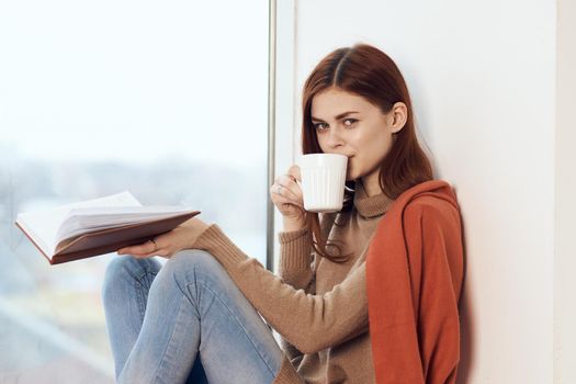 woman with a book near the window with a cup of coffee. High quality photo